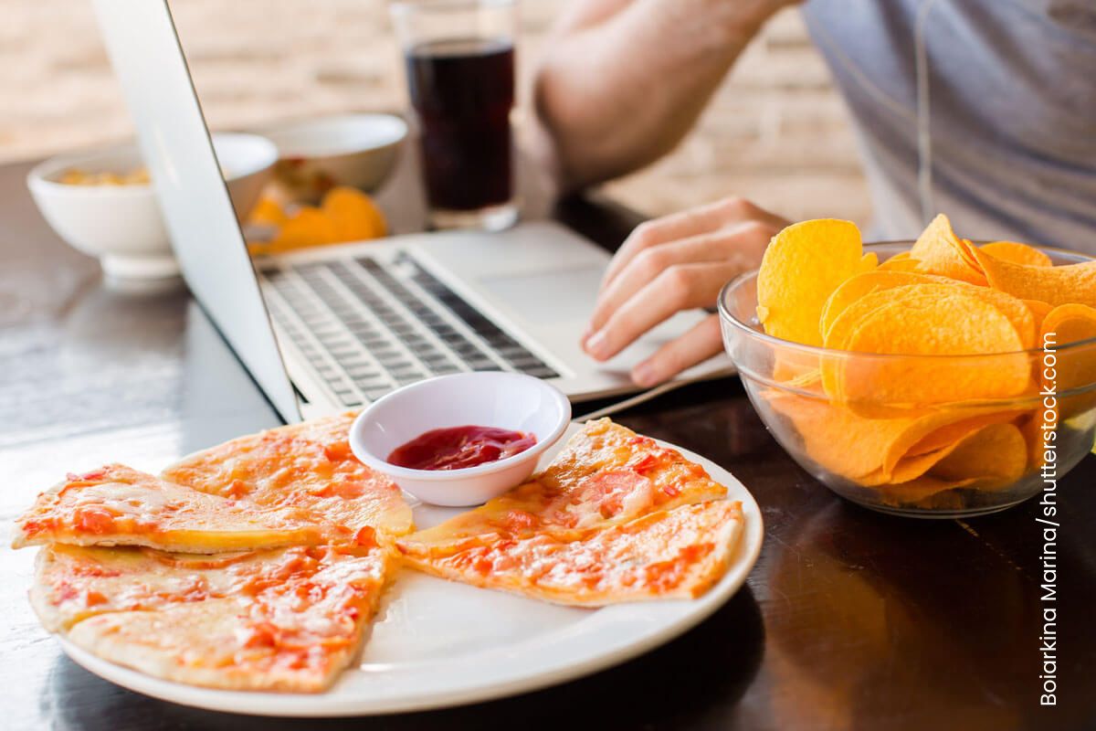 Person arbeitet an einem Laptop, Chips und Pizza neben sich. Für Diebetiker ist ein ungesunder Lebensstil noch ungünstiger als für andere.