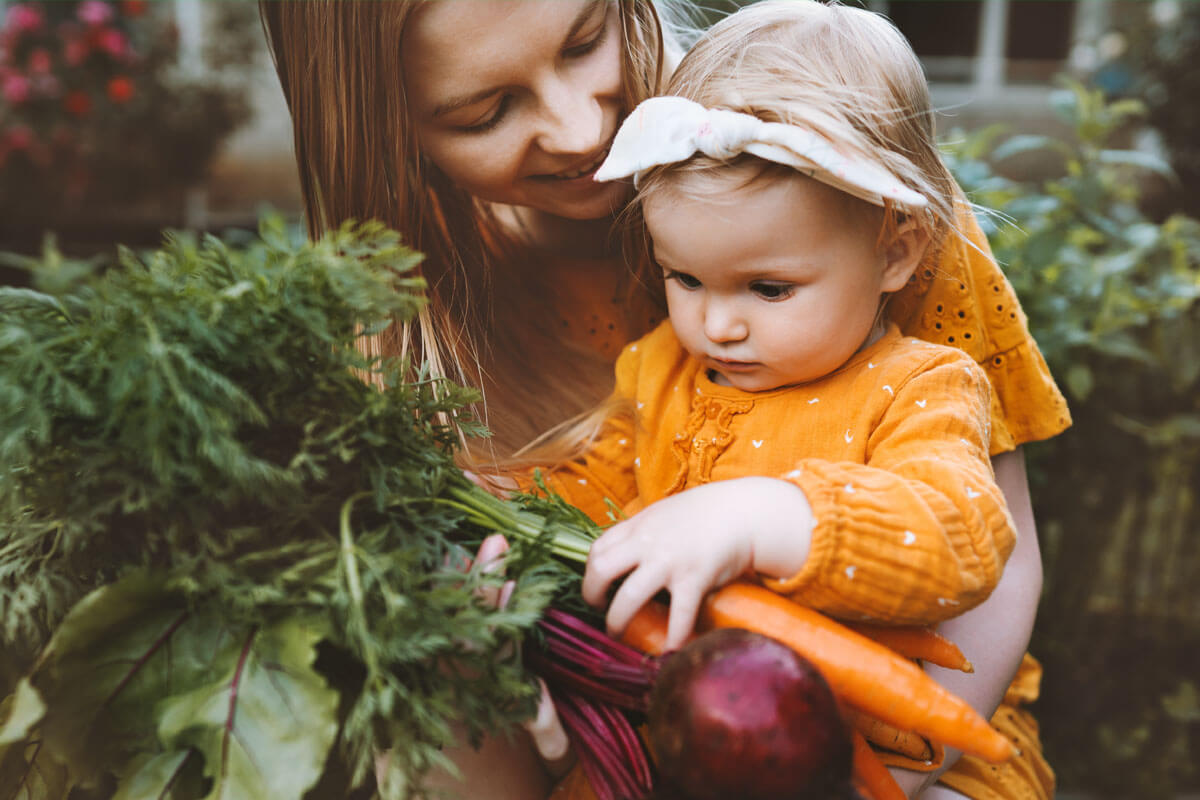 Mutter und Kind mit frisch geernteter Karotte. Bei aller Begeisterung für Veganismus dürfen gerade bei Kindern die Vitamine nicht vergessen werden.